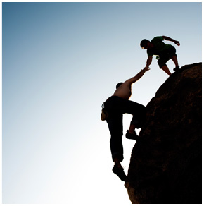 A man helping another climb a rock