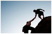 A man helping another climb on a rock