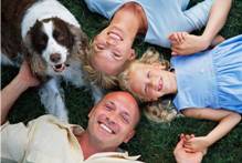 A family and a dog lying on the grass, holding hands